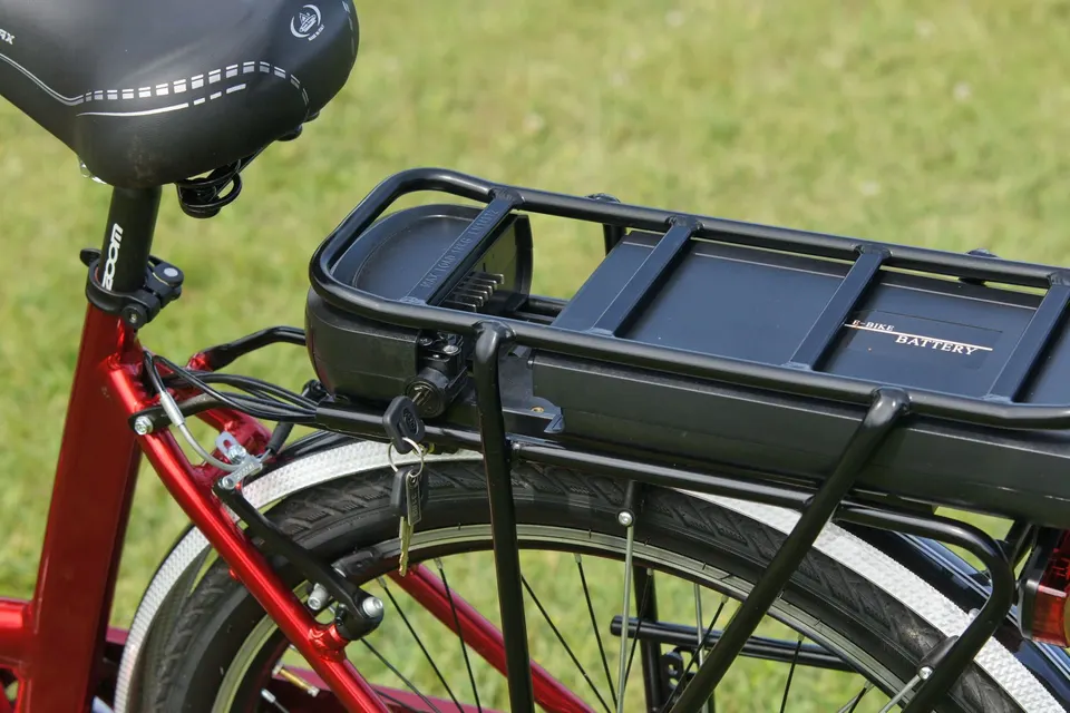 Batterie de vélo électrique fixée sous le porte-bagages d’un vélo de ville rouge, la clé dans la serrure