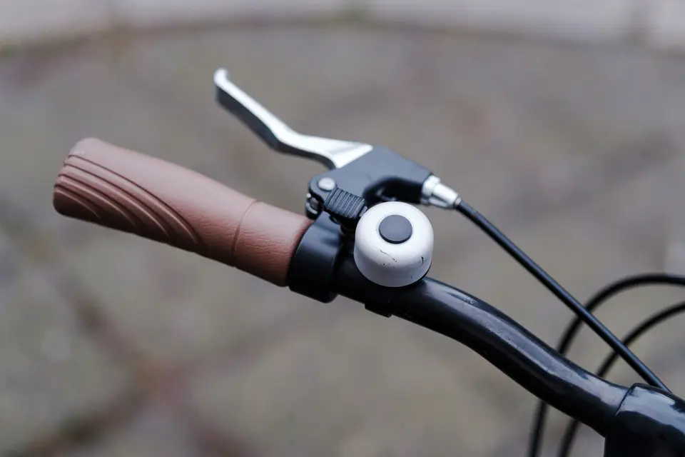Levier de frein et sonnette sur un cintre de vélo, le câble de frein partant du levier