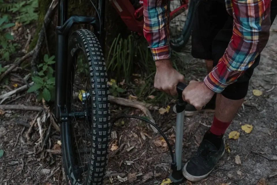 Cycliste gonflant à la pompe à pied le pneu à crampons d’un VTT, en forêt