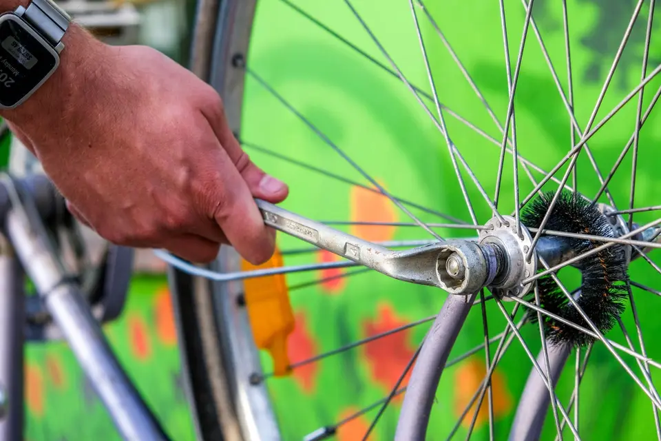Main serrant l’écrou d’axe d’une roue de vélo avec une clé, au milieu des rayons