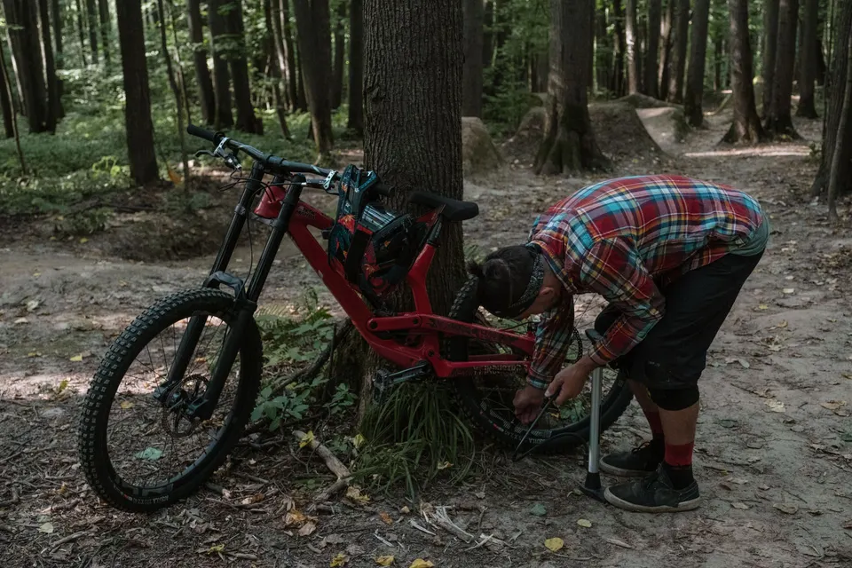 Vététiste en chemise à carreaux qui gonfle le pneu de son VTT avec une pompe à pied, en forêt