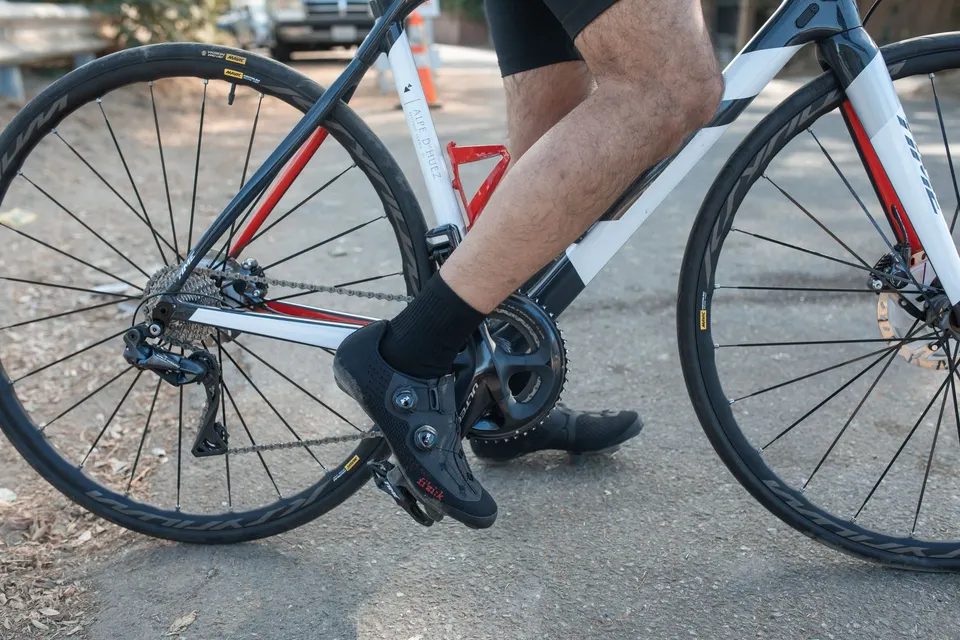 Cycliste en chaussures de route enclenchées dans des pédales automatiques, sur un vélo de route blanc