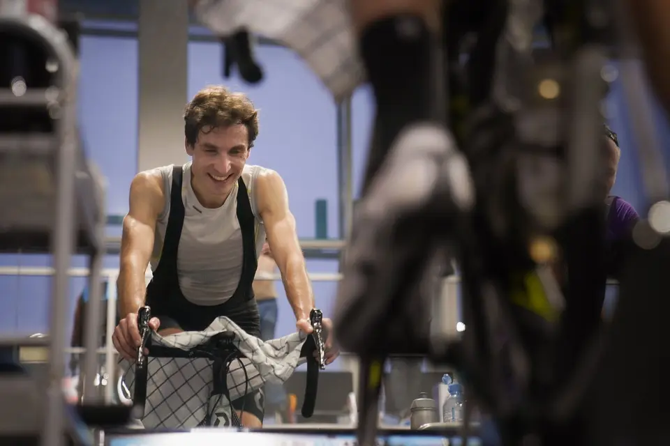 Cycliste souriant pendant une séance sur home-trainer, une serviette posée sur le cintre