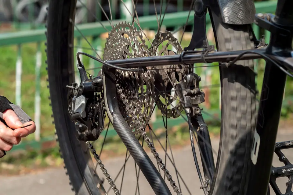 Main tenant une clé Allen près du dérailleur arrière et de la cassette d’un VTT