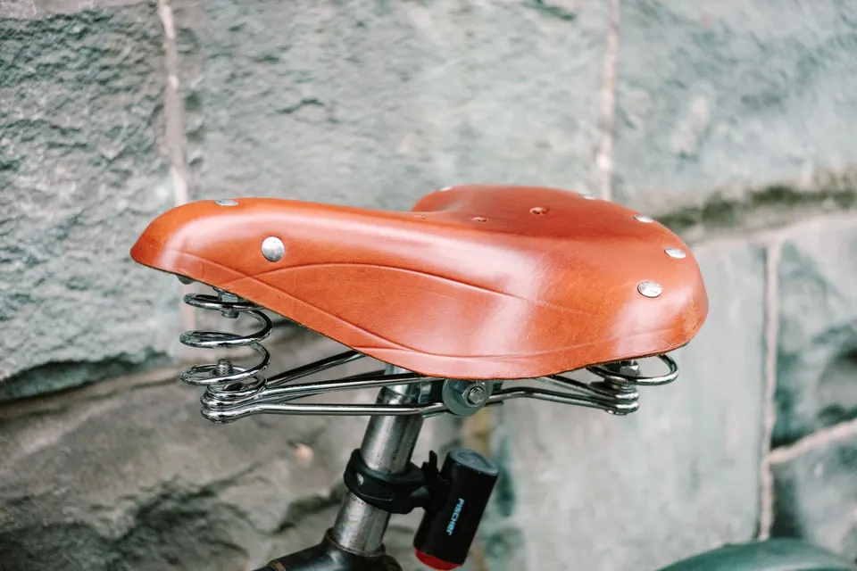 Selle de vélo en cuir couleur cognac montée sur ressorts, devant un mur de pierre