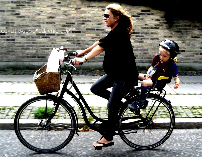 Femme enceinte faisant du vélo avec son autre enfant à l'arrière sur porte vélo.