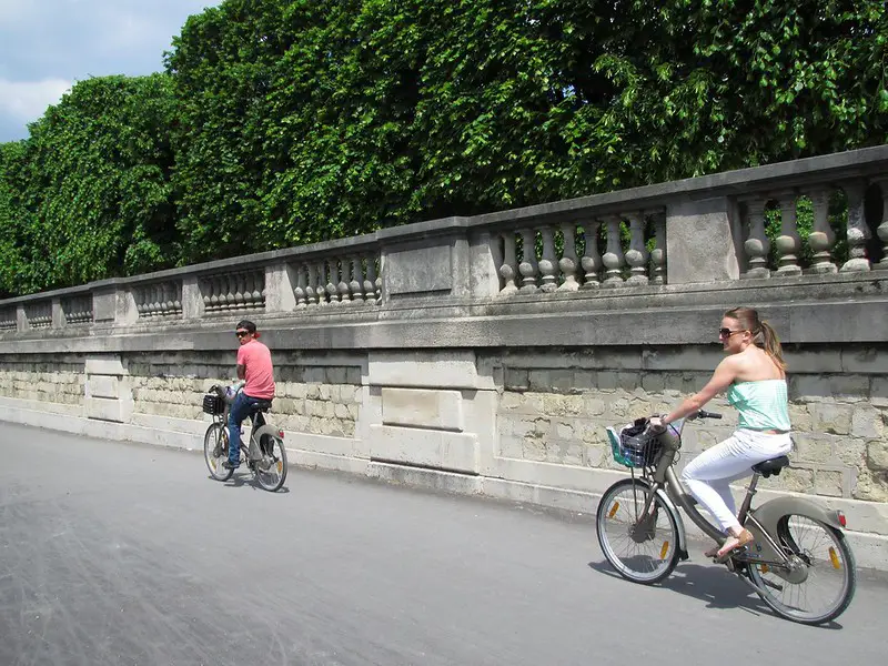 Deux personnes en vélo le long d'un jardin à Paris.